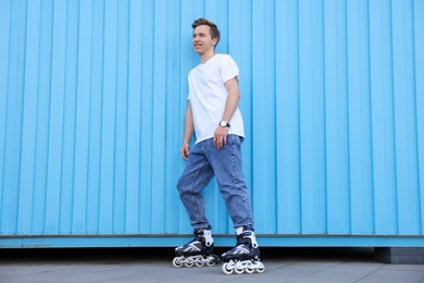 Photo of Happy young man with roller skates near light blue wall outdoors
