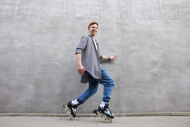 Photo of Happy young man roller skating near gray wall outdoors