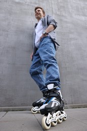 Photo of Happy young man with roller skates near gray wall outdoors, low angle view