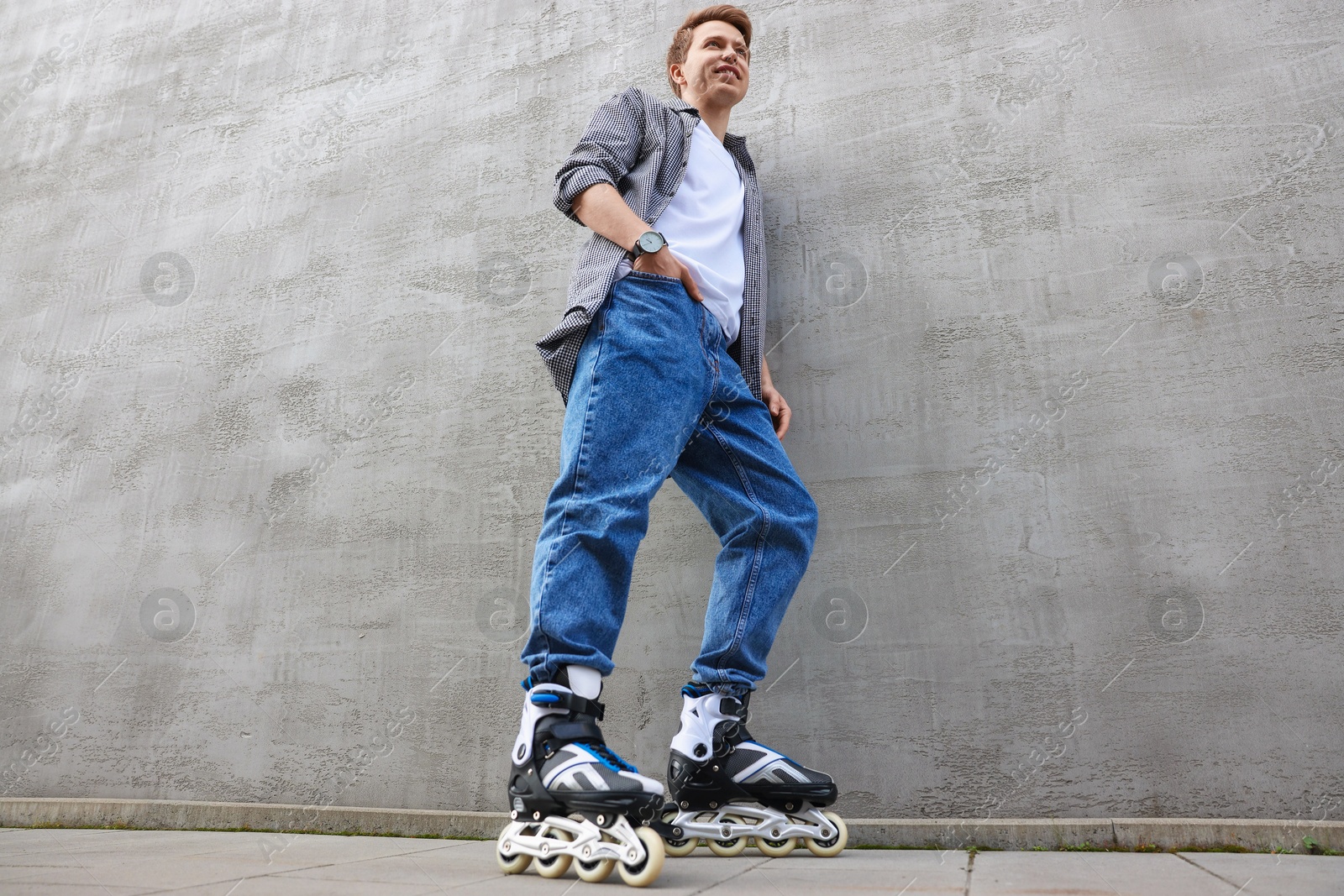 Photo of Happy young man with roller skates near gray wall outdoors, low angle view