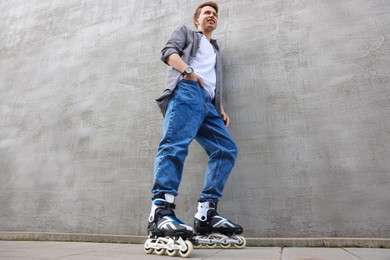 Photo of Happy young man with roller skates near gray wall outdoors, low angle view