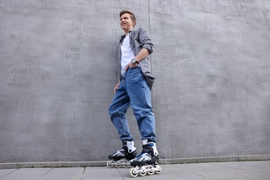 Photo of Happy young man with roller skates near gray wall outdoors, low angle view