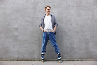 Photo of Happy young man with roller skates near gray wall outdoors