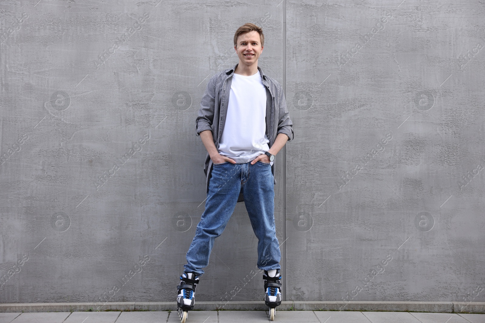 Happy young man with roller skates near gray wall outdoors Photo of Happy young man with roller skates near gray wall outdoors