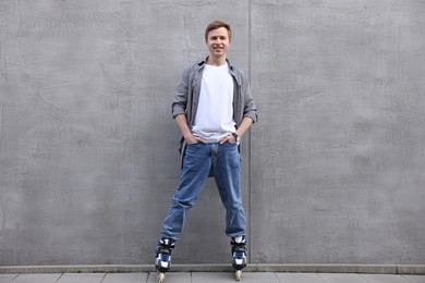Photo of Happy young man with roller skates near gray wall outdoors