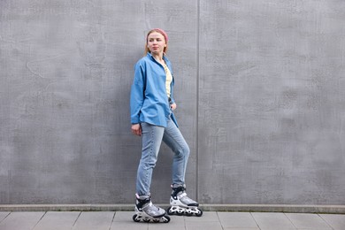 Photo of Beautiful young woman with roller skates near gray wall outdoors