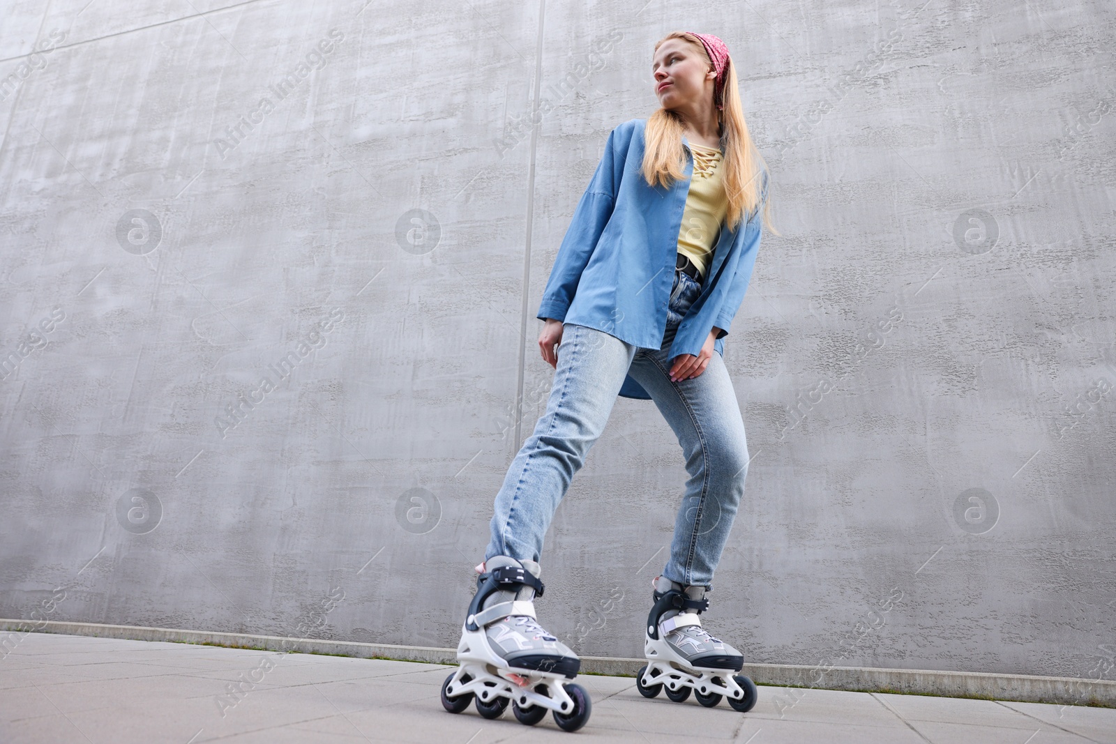 Photo of Beautiful young woman with roller skates near gray wall outdoors, low angle view