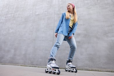 Photo of Beautiful young woman with roller skates near gray wall outdoors, low angle view