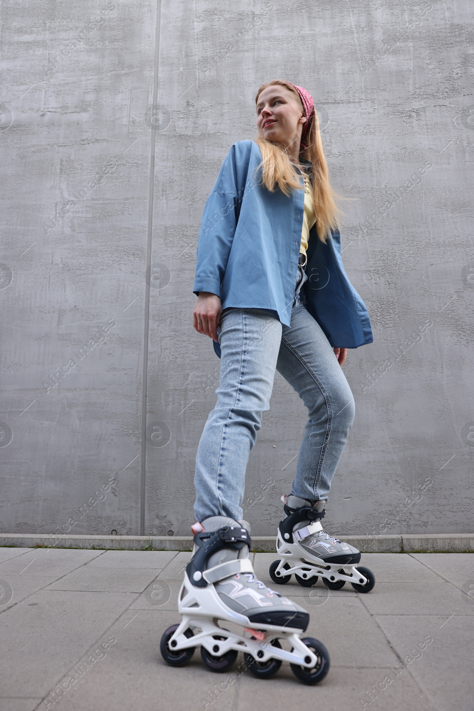 Photo of Beautiful young woman with roller skates near gray wall outdoors, low angle view