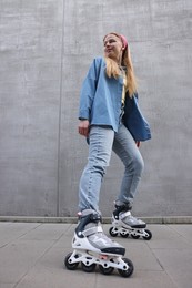 Photo of Beautiful young woman with roller skates near gray wall outdoors, low angle view