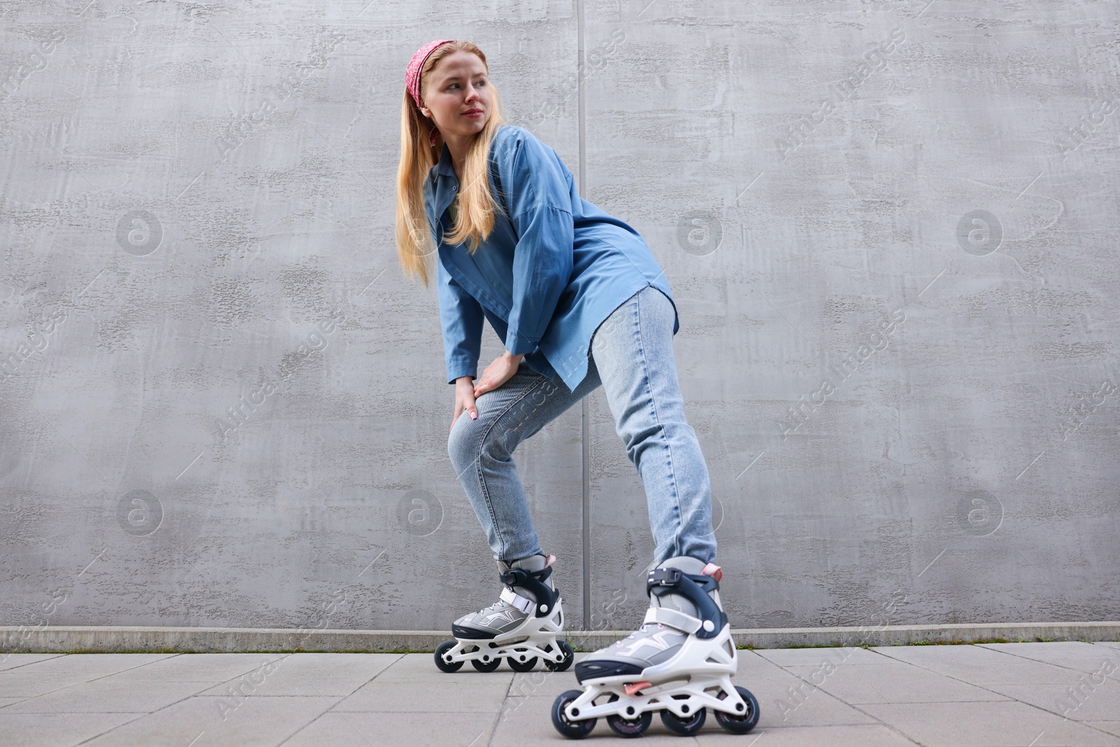 Beautiful young woman with roller skates near gray wall outdoors, low angle view Photo of Beautiful young woman with roller skates near gray wall outdoors, low angle view