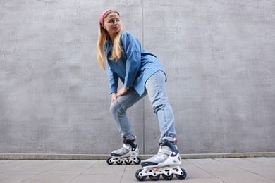 Photo of Beautiful young woman with roller skates near gray wall outdoors, low angle view