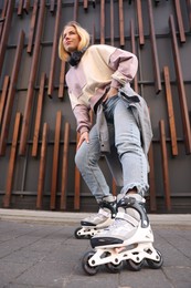Photo of Beautiful young woman with roller skates near building outdoors, low angle view