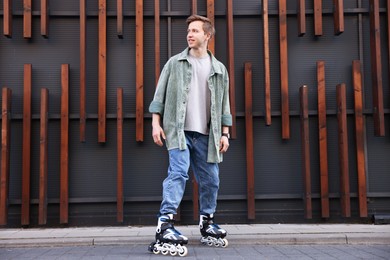 Photo of Happy young man with roller skates near building outdoors