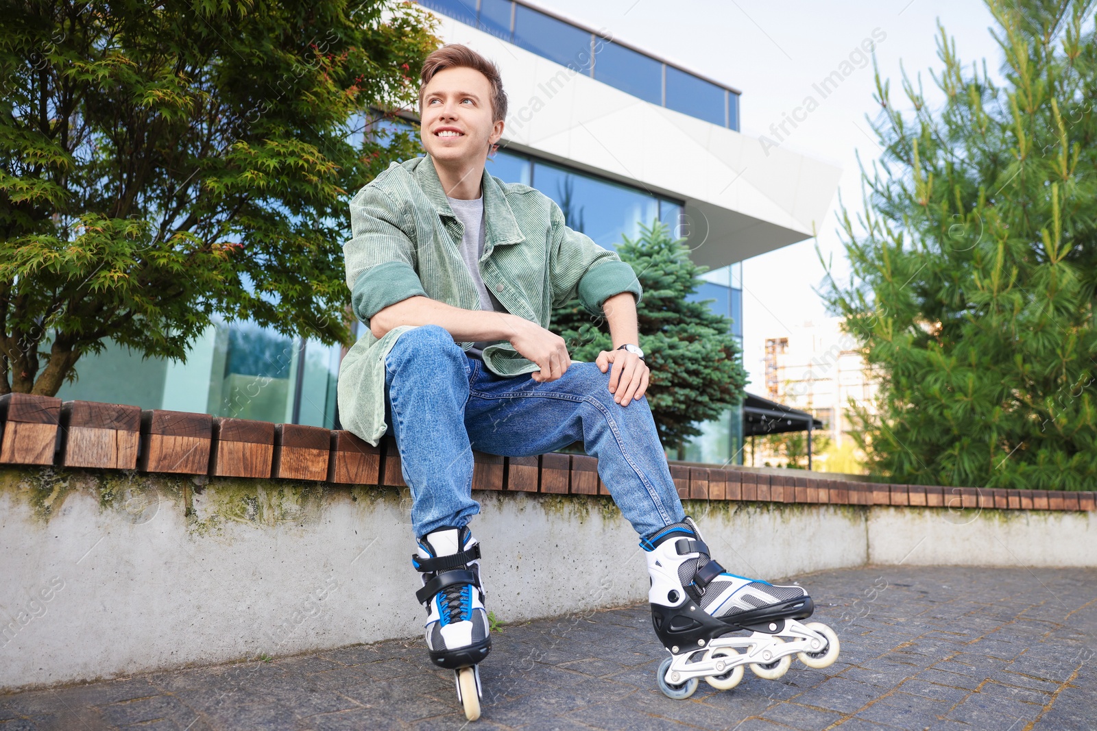 Young man with roller skates on wooden bench outdoors Photo of Young man with roller skates on wooden bench outdoors