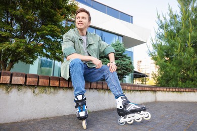 Photo of Young man with roller skates on wooden bench outdoors