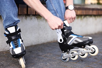 Photo of Young man putting on roller skates outdoors, closeup