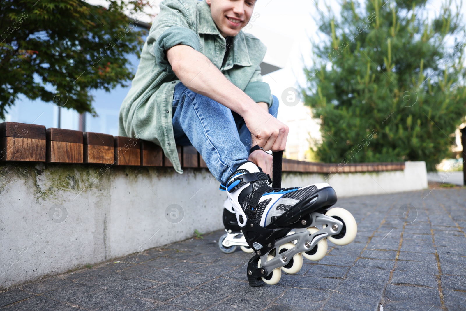 Happy young man putting on roller skates outdoors, selective focus Photo of Happy young man putting on roller skates outdoors, selective focus