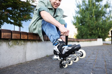 Photo of Happy young man putting on roller skates outdoors, selective focus