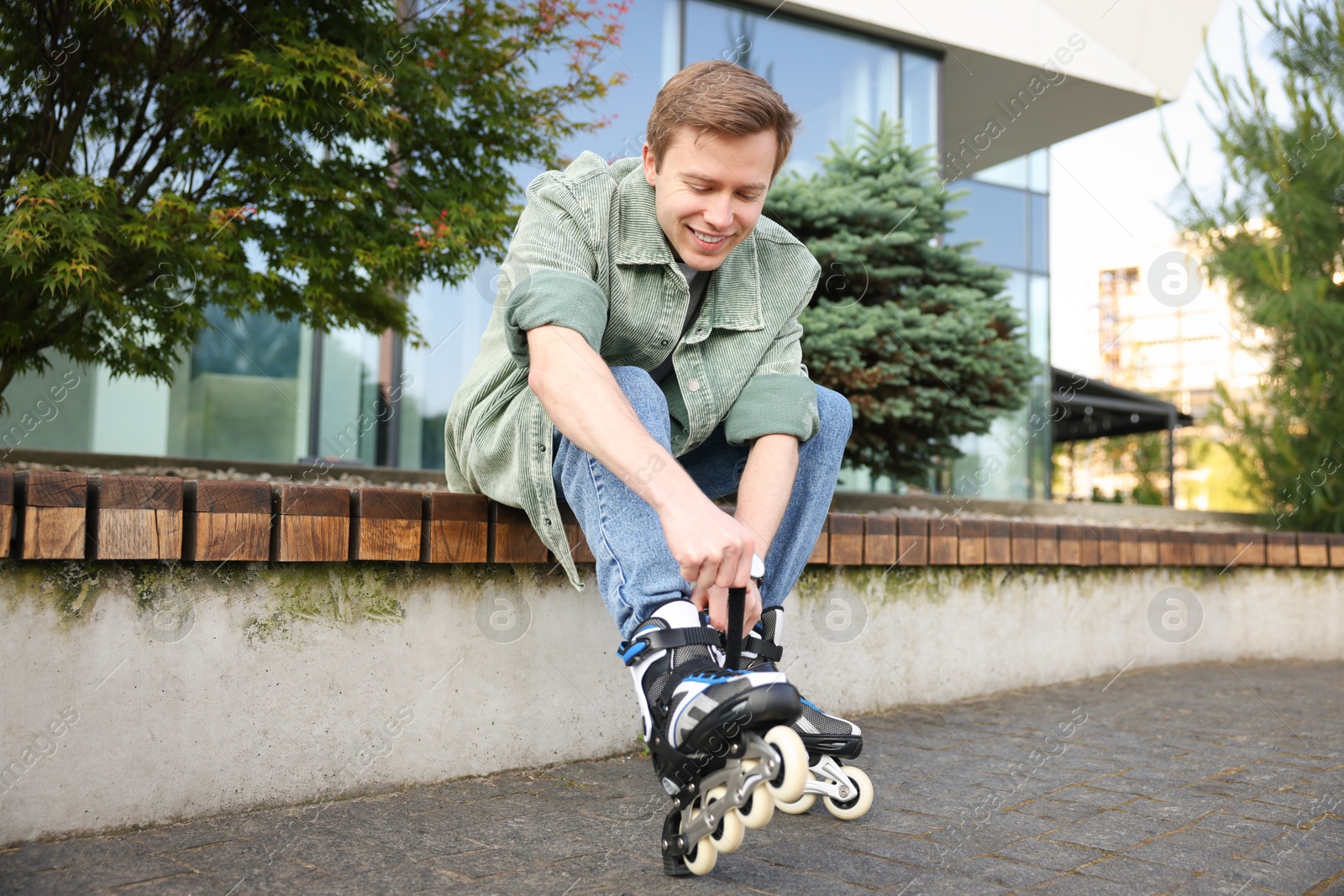 Happy young man putting on roller skates outdoors Photo of Happy young man putting on roller skates outdoors