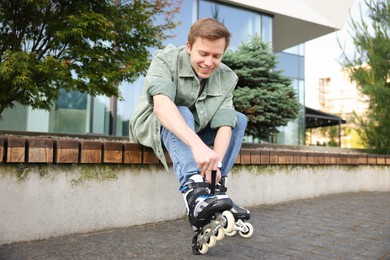Photo of Happy young man putting on roller skates outdoors