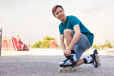 Photo of Happy man putting on roller skates outdoors