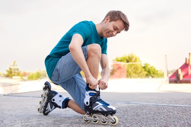 Photo of Happy man putting on roller skates outdoors