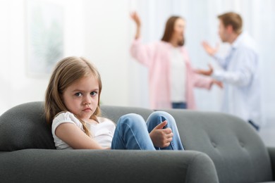 Photo of Upset little girl on sofa and her parents fighting at home, selective focus