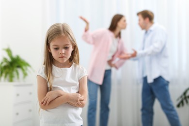 Photo of Upset little girl and her parents fighting at home, selective focus