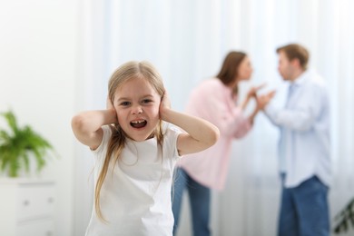 Photo of Upset little girl and her parents fighting at home, selective focus