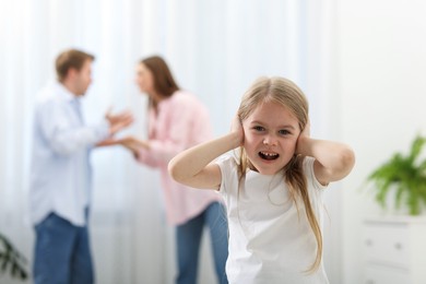 Photo of Upset little girl and her parents fighting at home, selective focus