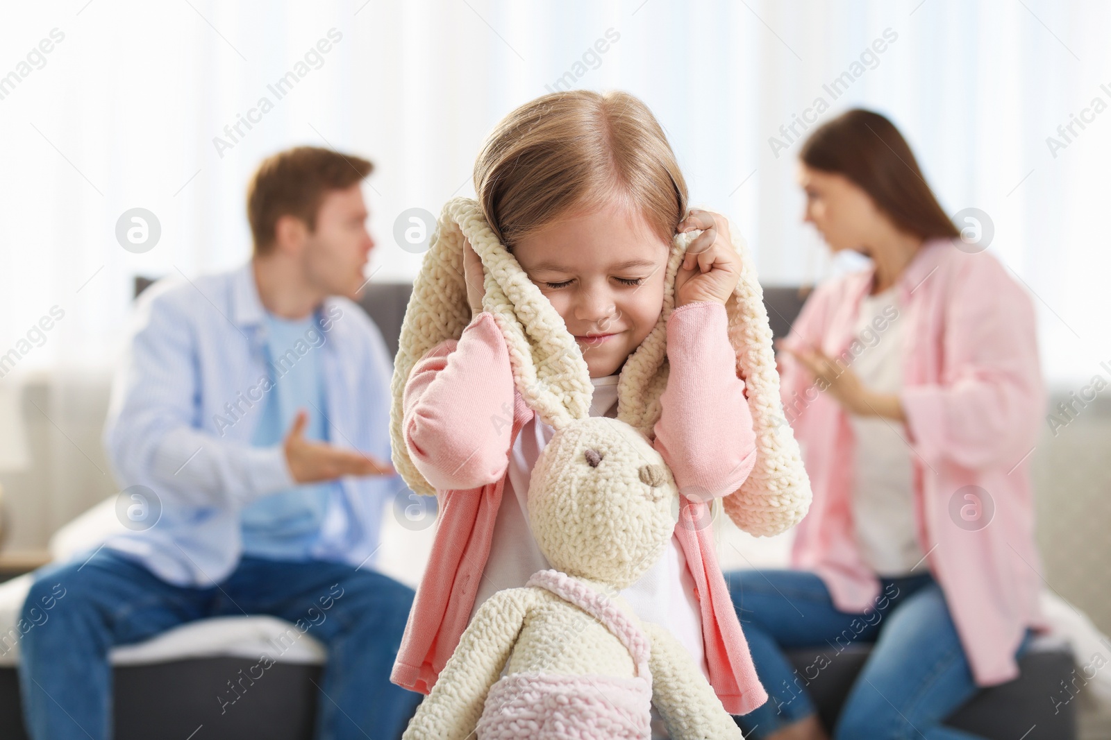 Upset little girl with bunny and her parents fighting at home, selective focus Photo of Upset little girl with bunny and her parents fighting at home, selective focus