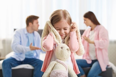 Photo of Upset little girl with bunny and her parents fighting at home, selective focus