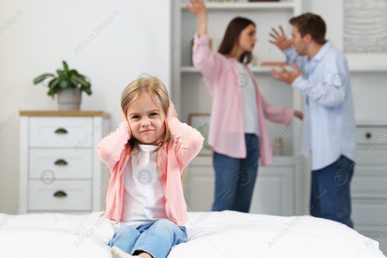 Upset little girl on bed and her parents fighting at home, selective focus Photo of Upset little girl on bed and her parents fighting at home, selective focus