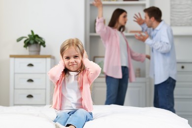 Photo of Upset little girl on bed and her parents fighting at home, selective focus