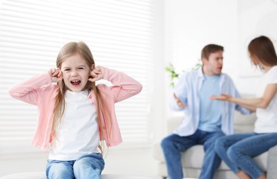 Photo of Upset little girl and her parents fighting at home, selective focus