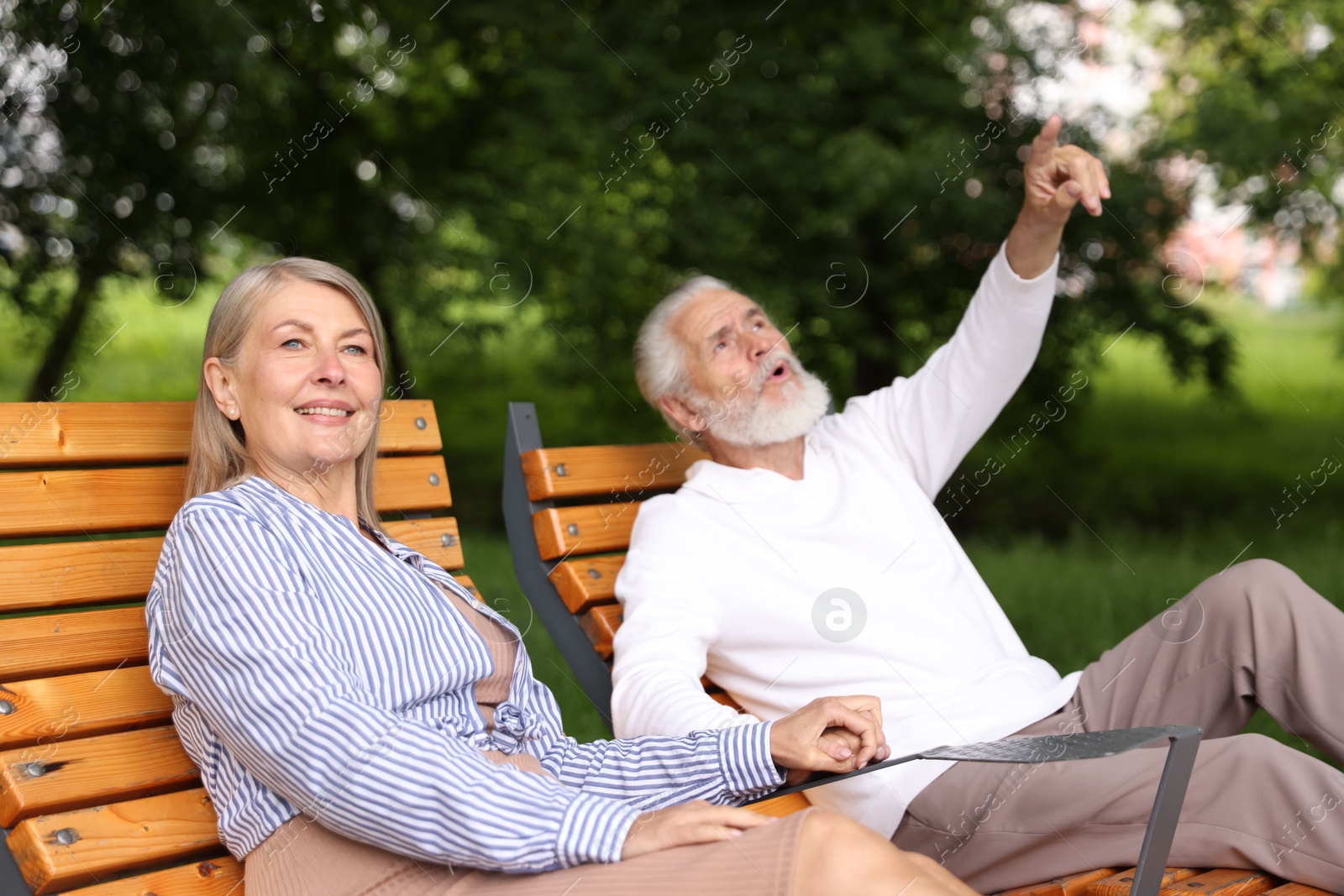 Photo of Lovely senior couple resting on wooden sunbeds in park