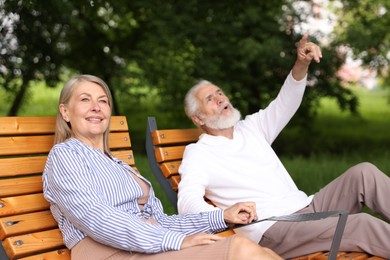 Photo of Lovely senior couple resting on wooden sunbeds in park
