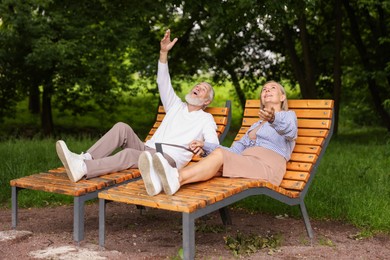 Photo of Lovely senior couple resting on wooden sunbeds in park