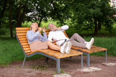 Photo of Lovely senior couple resting on wooden sunbeds in park