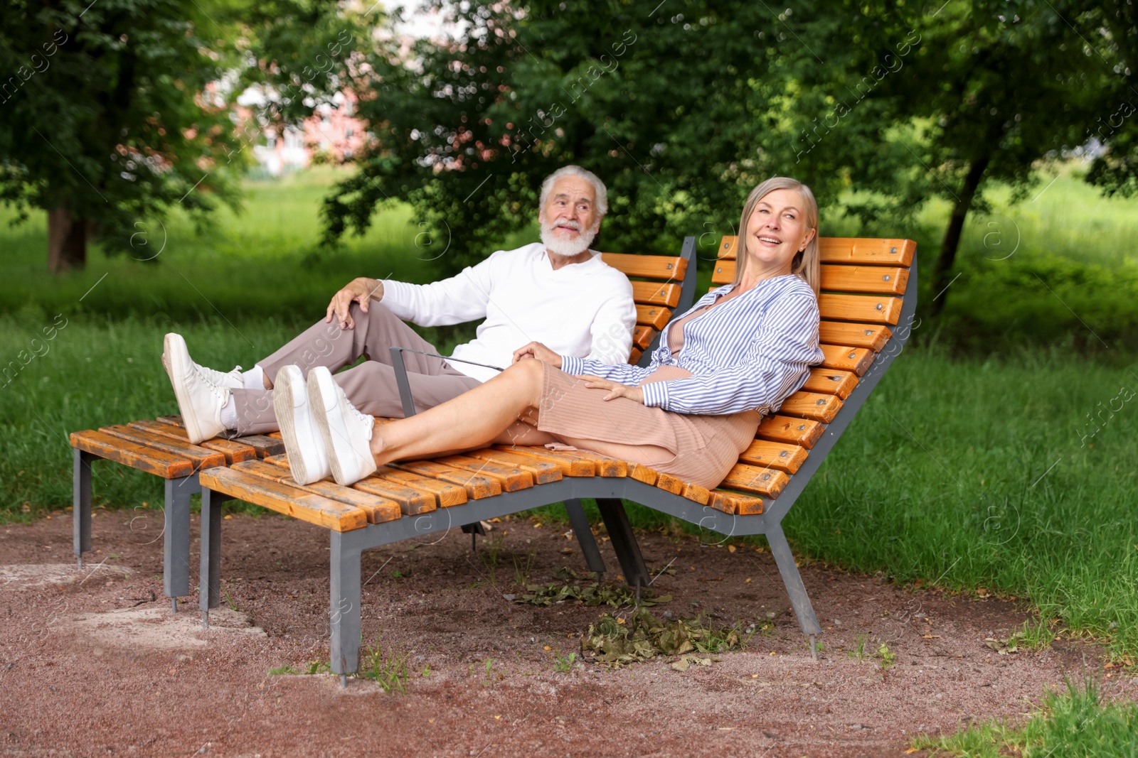 Photo of Lovely senior couple resting on wooden sunbeds in park
