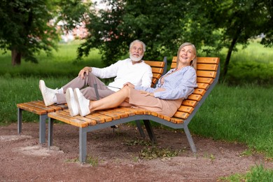 Photo of Lovely senior couple resting on wooden sunbeds in park