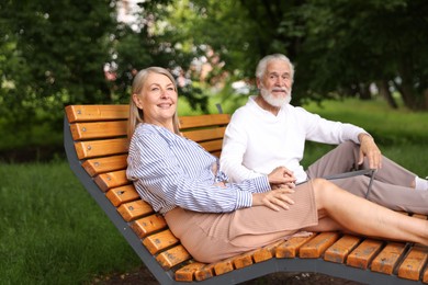Photo of Lovely senior couple resting on wooden sunbeds in park