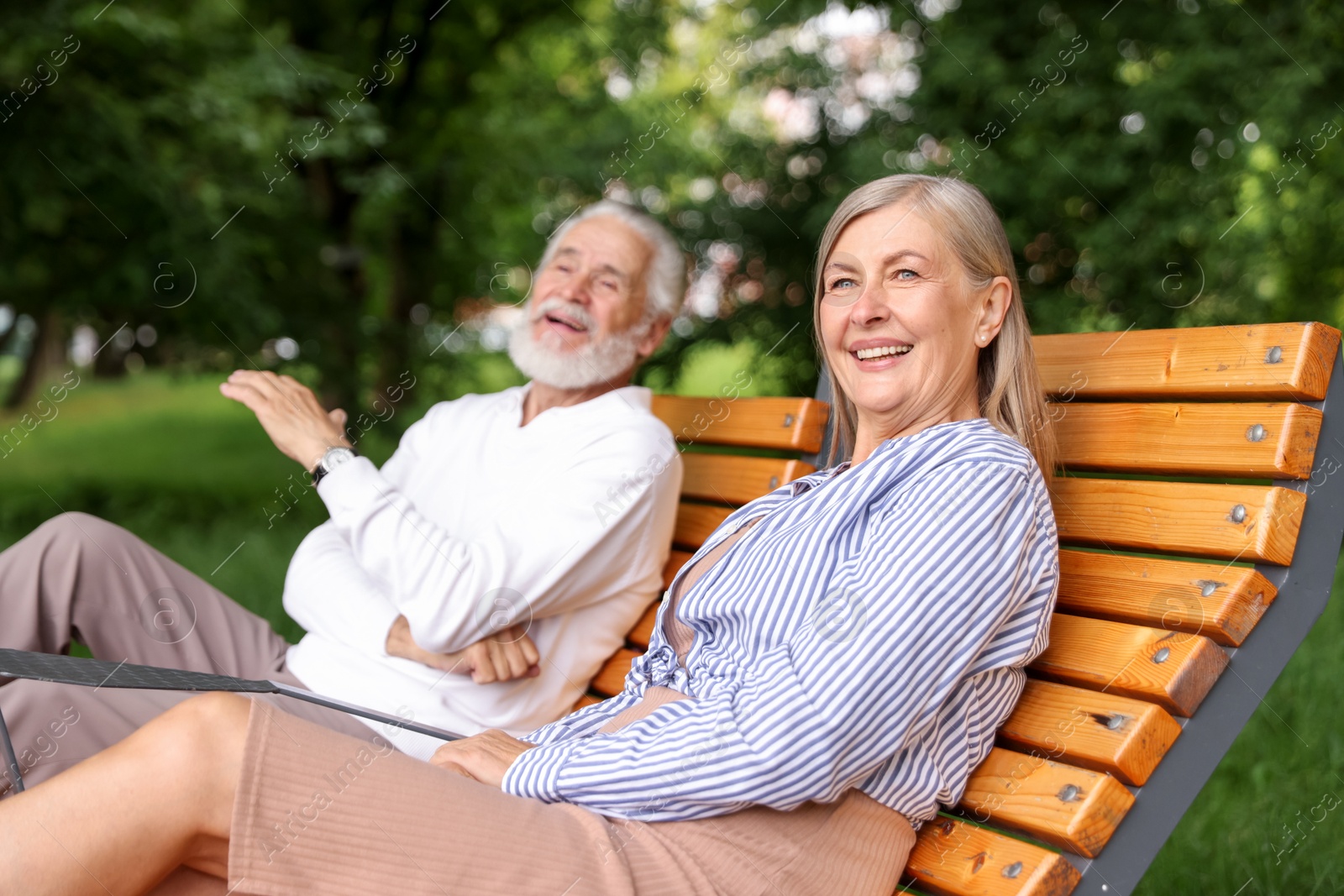 Photo of Lovely senior couple resting on wooden sunbeds in park