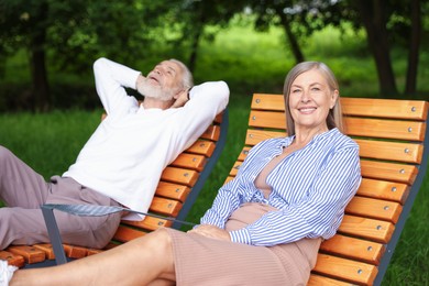 Photo of Lovely senior couple resting on wooden sunbeds in park