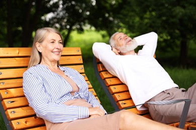 Photo of Lovely senior couple resting on wooden sunbeds in park