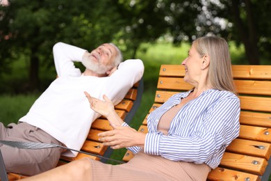 Photo of Lovely senior couple resting on wooden sunbeds in park