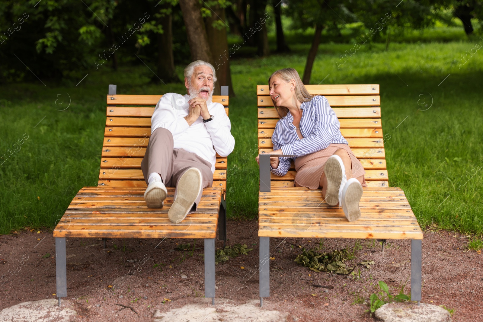 Photo of Lovely senior couple resting on wooden sunbeds in park
