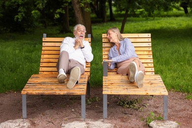 Photo of Lovely senior couple resting on wooden sunbeds in park