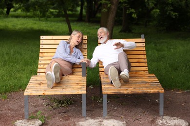 Photo of Lovely senior couple resting on wooden sunbeds in park